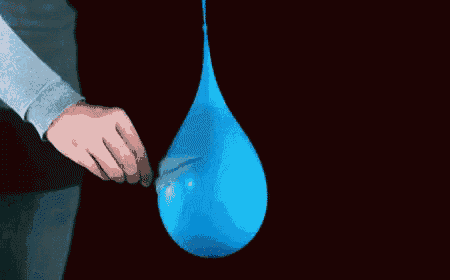 a person is blowing up a blue water balloon with a black background