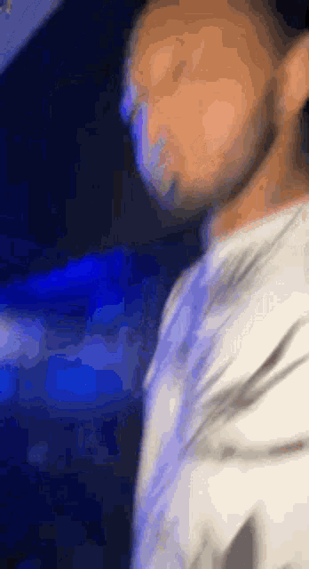 a blurry picture of a man in a white shirt standing in a dark room .
