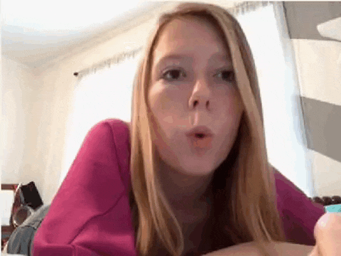 a young girl in a pink shirt is blowing a bubble .