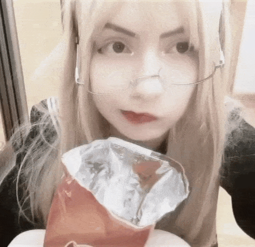a girl wearing glasses and a nose ring is eating a bag of potato chips .