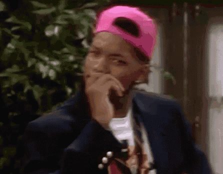 a man wearing a pink hat and a suit is covering his mouth with his hands .