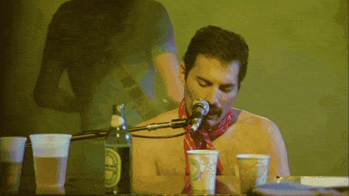 a shirtless man singing into a microphone next to a bottle of heineken