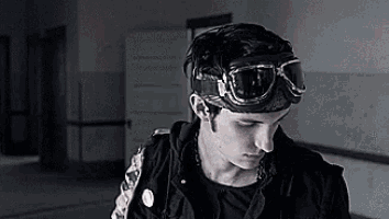 a young man wearing a black jacket and goggles looks down