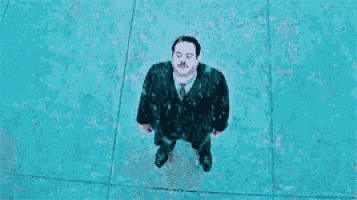 an aerial view of a man in a suit and tie standing on a sidewalk .