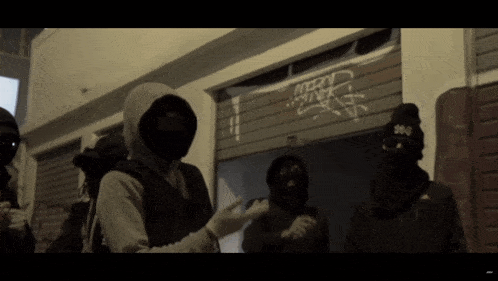 a group of people wearing masks are standing in front of a building with graffiti on it that says mory wink