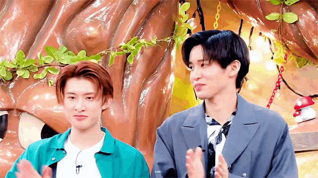 two young men standing next to each other in front of a statue of a tree .