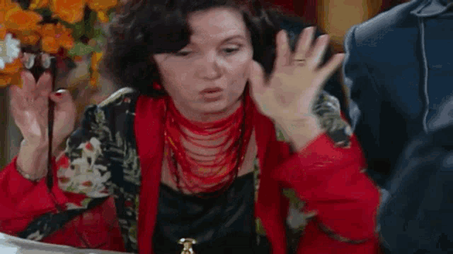 a woman in a red cardigan is holding a magnifying glass and talking to a man