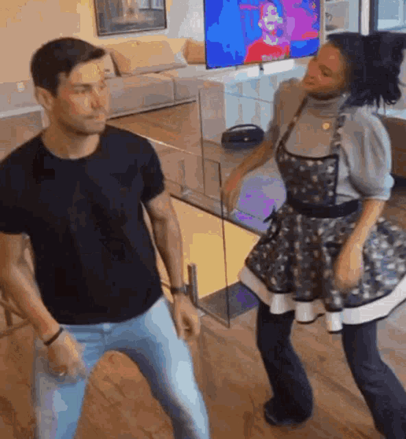 a man and a woman are dancing in a living room with a television in the background .