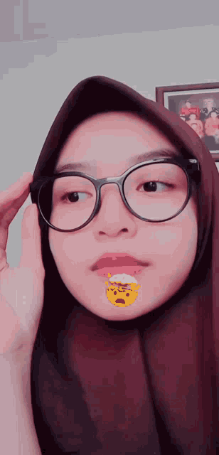 a woman wearing glasses and a hijab has a yellow smiley face on her face