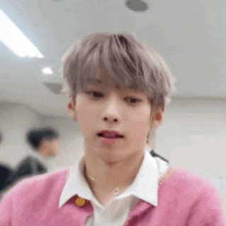 a young man wearing a pink sweater and a white shirt is making a funny face .