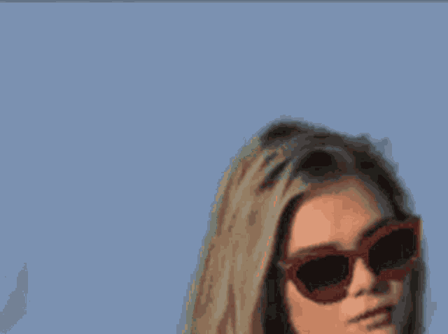 a woman wearing sunglasses is standing in front of a blue sky
