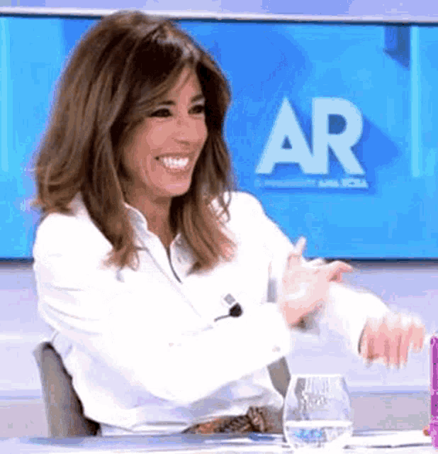 a woman in a white shirt is sitting at a table with a glass of water in front of a screen that says ar