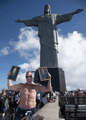 a shirtless man stands in front of a large statue of jesus