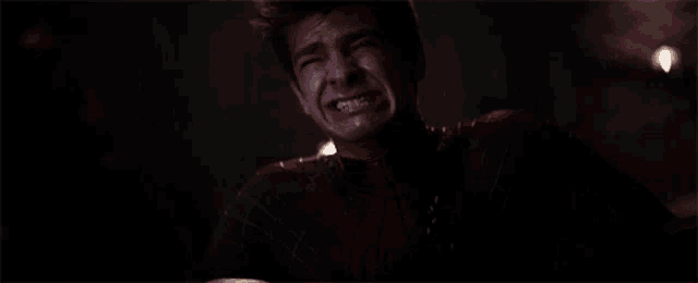 a man in a spiderman suit is screaming with his mouth open in a dark room .