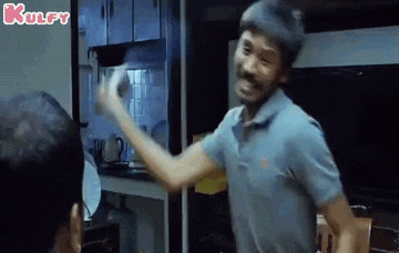 a man in a blue shirt is standing in a kitchen holding a cup .