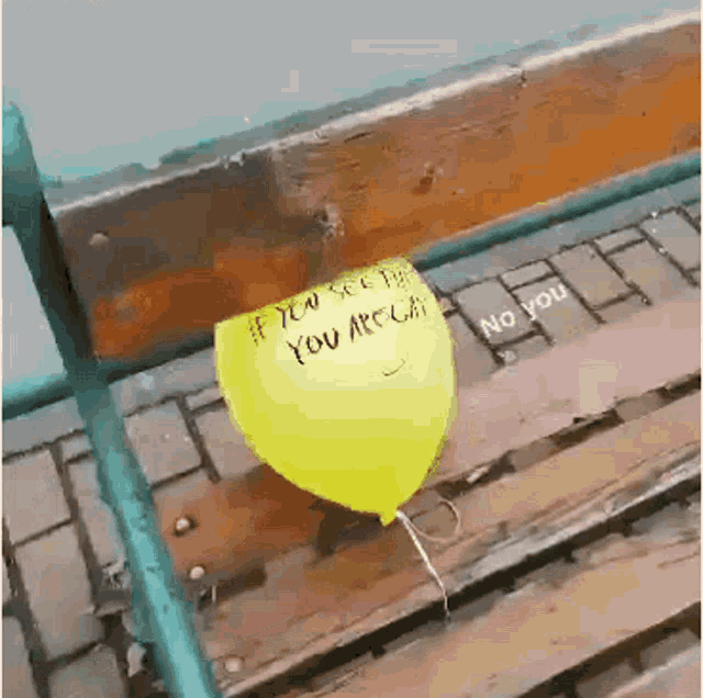 a yellow balloon with the words if you see the you are gay written on it is sitting on a wooden bench