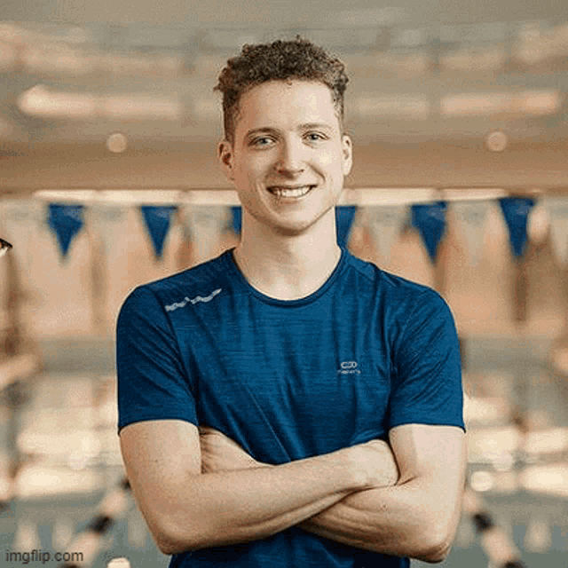 a young man in a blue shirt is standing in front of a swimming pool with his arms crossed .