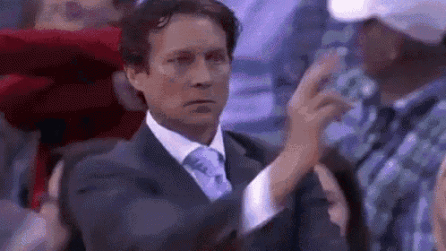 a man in a suit and tie is giving a thumbs up while sitting in a crowd .