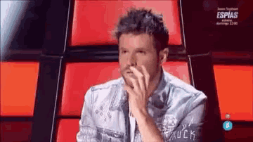 a man in a denim jacket is sitting in a red chair with his hands on his face