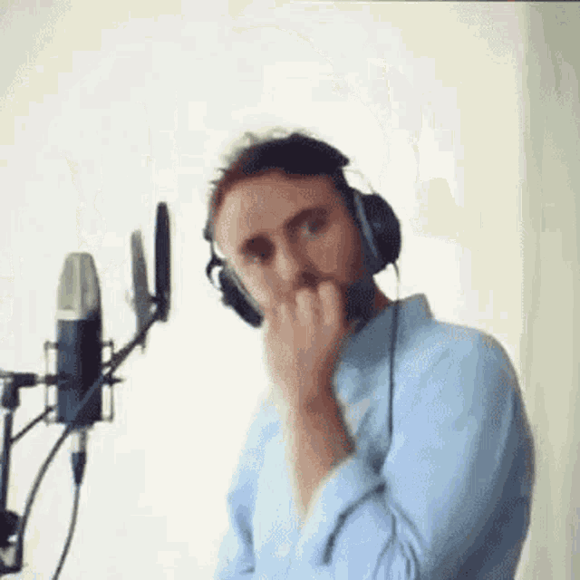 a man wearing headphones is standing in front of a microphone and covering his nose .