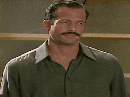 a man with a mustache and a green shirt looks down