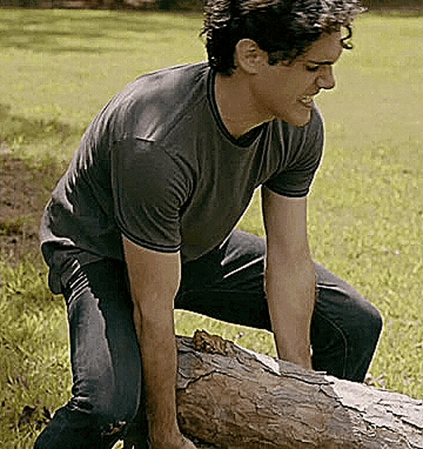 a man is kneeling down on a log in a field .