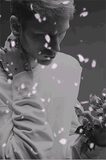 a black and white photo of a man holding a rose with pink petals falling around him