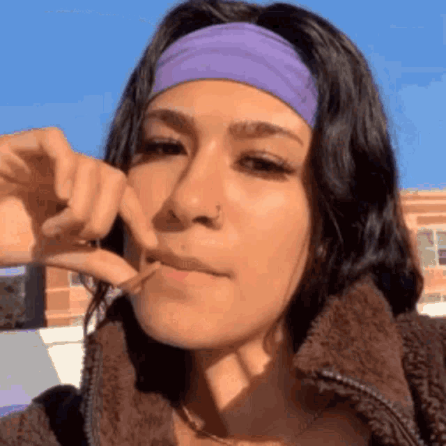a woman wearing a purple headband and a brown jacket is eating something .