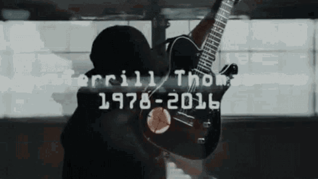 a man is holding a guitar in front of a sign that says terrill thomas 1978-2016
