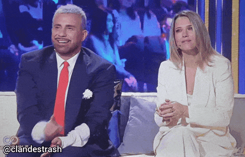 a man in a suit and tie sits next to a woman in a white dress