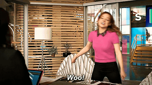 a woman in a pink shirt says woo while holding a piece of paper