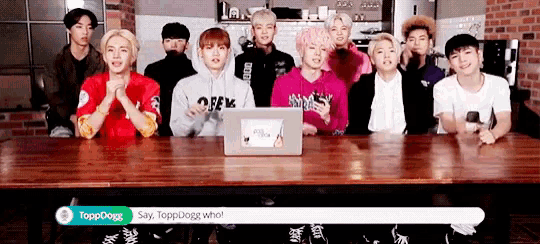 a group of young men are sitting at a table with a laptop on it and one of them is saying toppdogg who