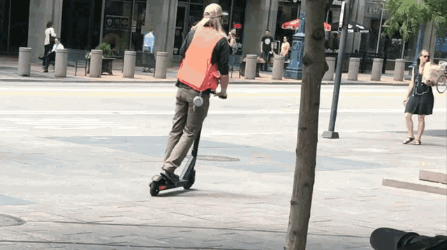 a man in an orange vest is riding a scooter on a street