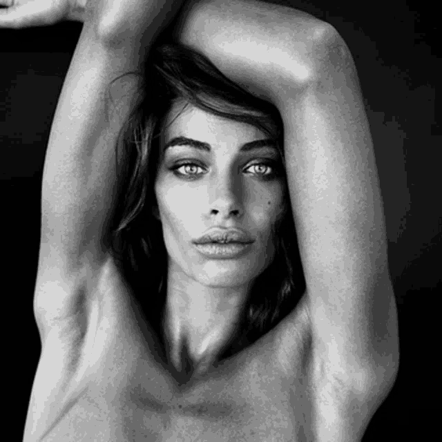 a black and white photo of a naked woman with her arms behind her head