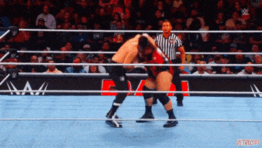 two men are wrestling in a ring with a referee watching