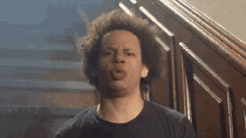a man with curly hair is making a funny face while standing in front of a wooden staircase .