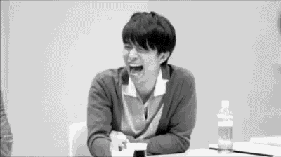 a man is laughing while sitting at a table with a bottle of water .