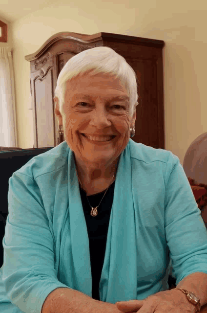 an older woman wearing a blue sweater and a black shirt smiles for the camera