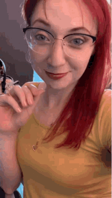 a woman with red hair and glasses is wearing a yellow shirt .