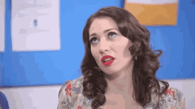 a woman with red lipstick is sitting in front of a blue wall and making a funny face .