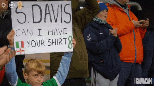 a young boy holds up a sign that says " 5 davis can i have your shirt "