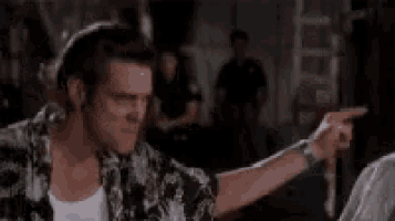 a man in a hawaiian shirt is pointing at someone in a room .