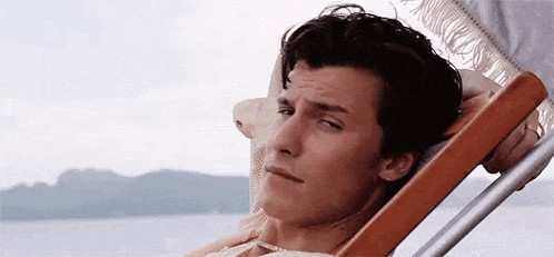 a young man is sitting in a beach chair with his head on the arm rest .