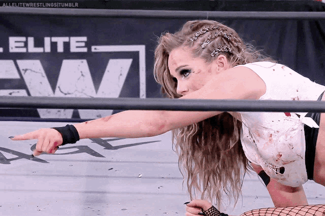 a female wrestler is pointing at something in front of a banner for elite wrestling