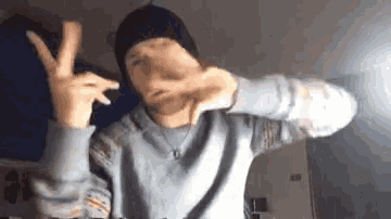 a young man wearing a hat and a sweater is making a peace sign with his hands .