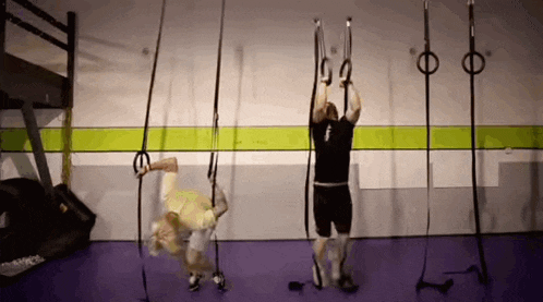 a man and a woman are doing exercises on gymnastic rings in a gym .