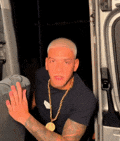 a man wearing a gold chain and a black shirt is sitting in the doorway of a van .