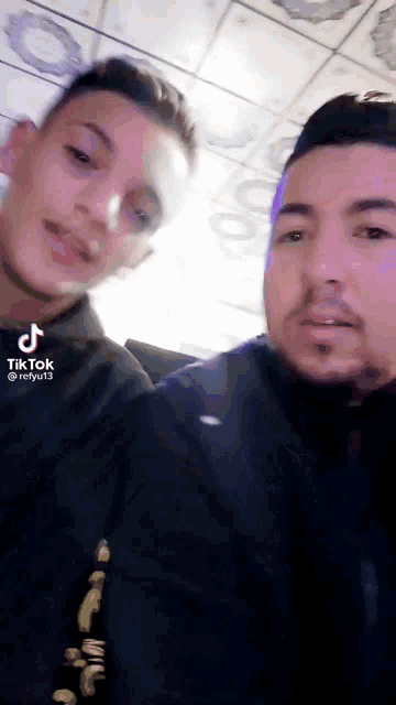 two men are posing for a picture and one of them has a tiktok on his phone