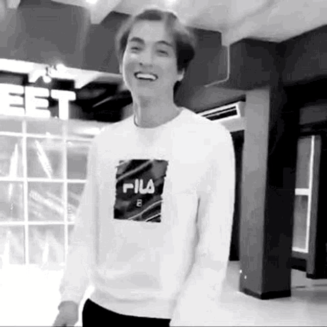 a black and white photo of a young man wearing a white fila sweatshirt .