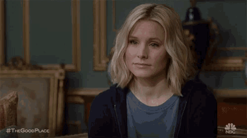 a woman is sitting in a room with a painting in the background and looking at the camera .